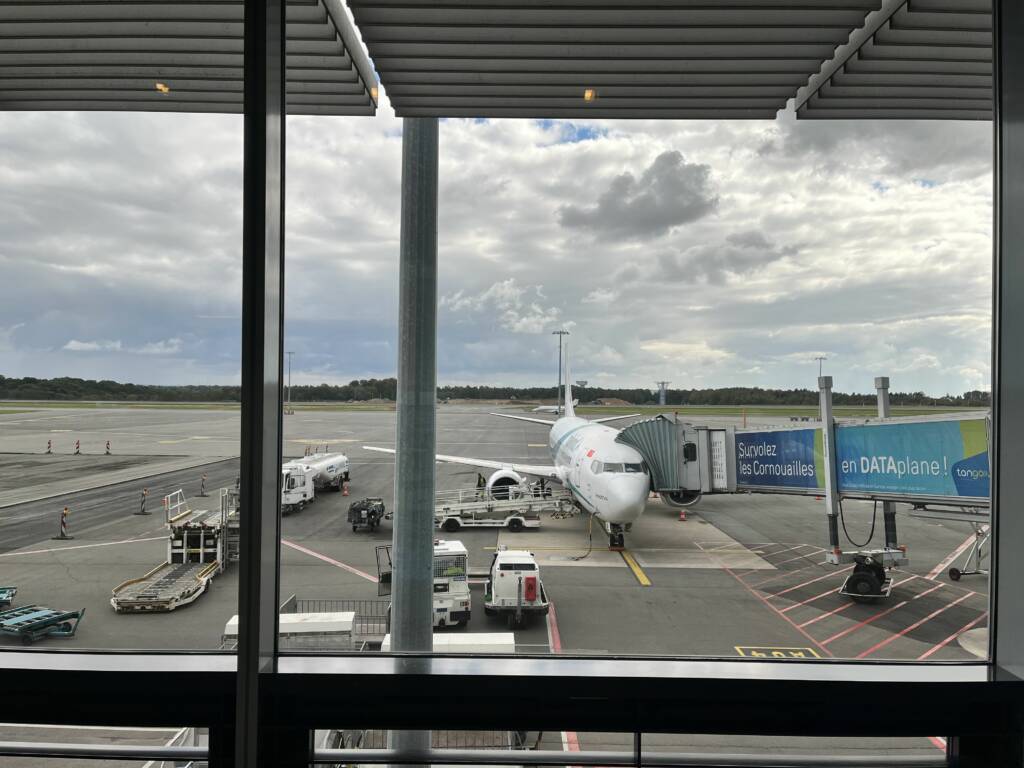 Avion blanc, type Boeing 737-400 de la compagnie aérienne Tailwind sur le tarmac de l'aéroport du Luxembourg. Une passerelle aéroportuaire est lié à l'avion, permettant aux passagers de monter à bord. 