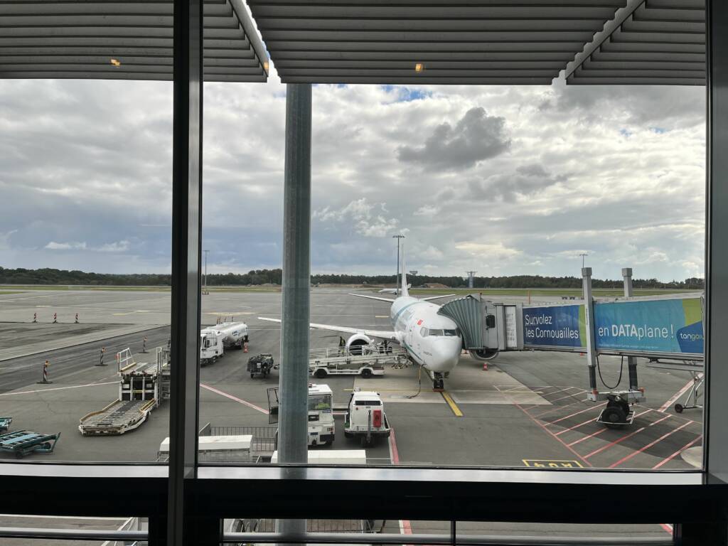 White plane, type Boeing 737-400 of the airline Tailwind on the tarmac of the airport of Luxembourg. An airport footbridge is linked to the plane, allowing passengers to board.